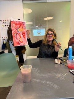 Smiling adult student holding up her finished painting at a Lea Art Studio workshop