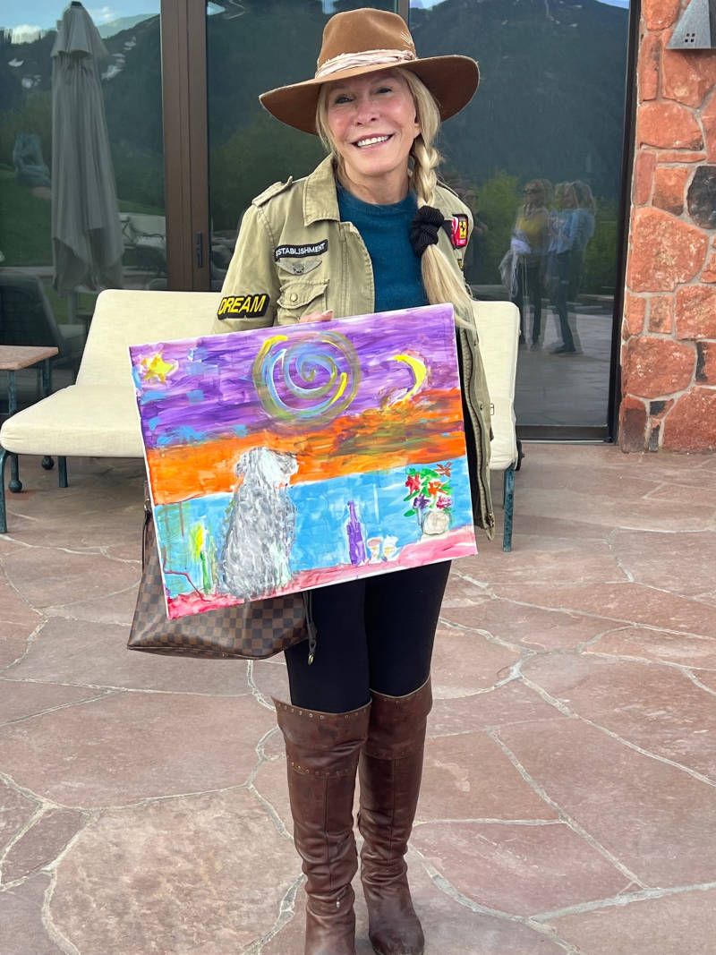 Woman with braided hair proudly holding her finished painting at a Lea Art Studio session